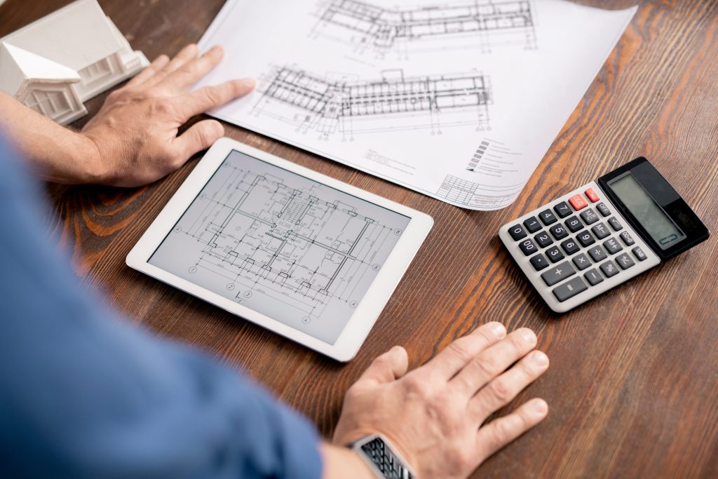 Hands of modern engineer leaning on wooden table while bending over tablet