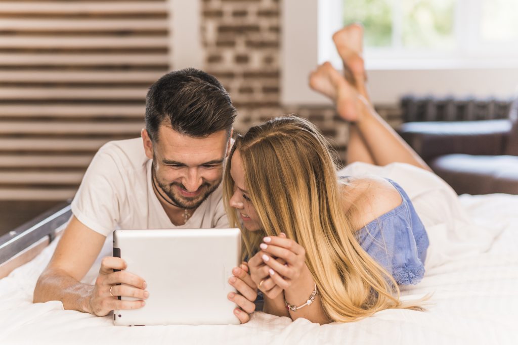 sonriente-joven-pareja-acostada-en-la-cama-mirando-tableta-digital